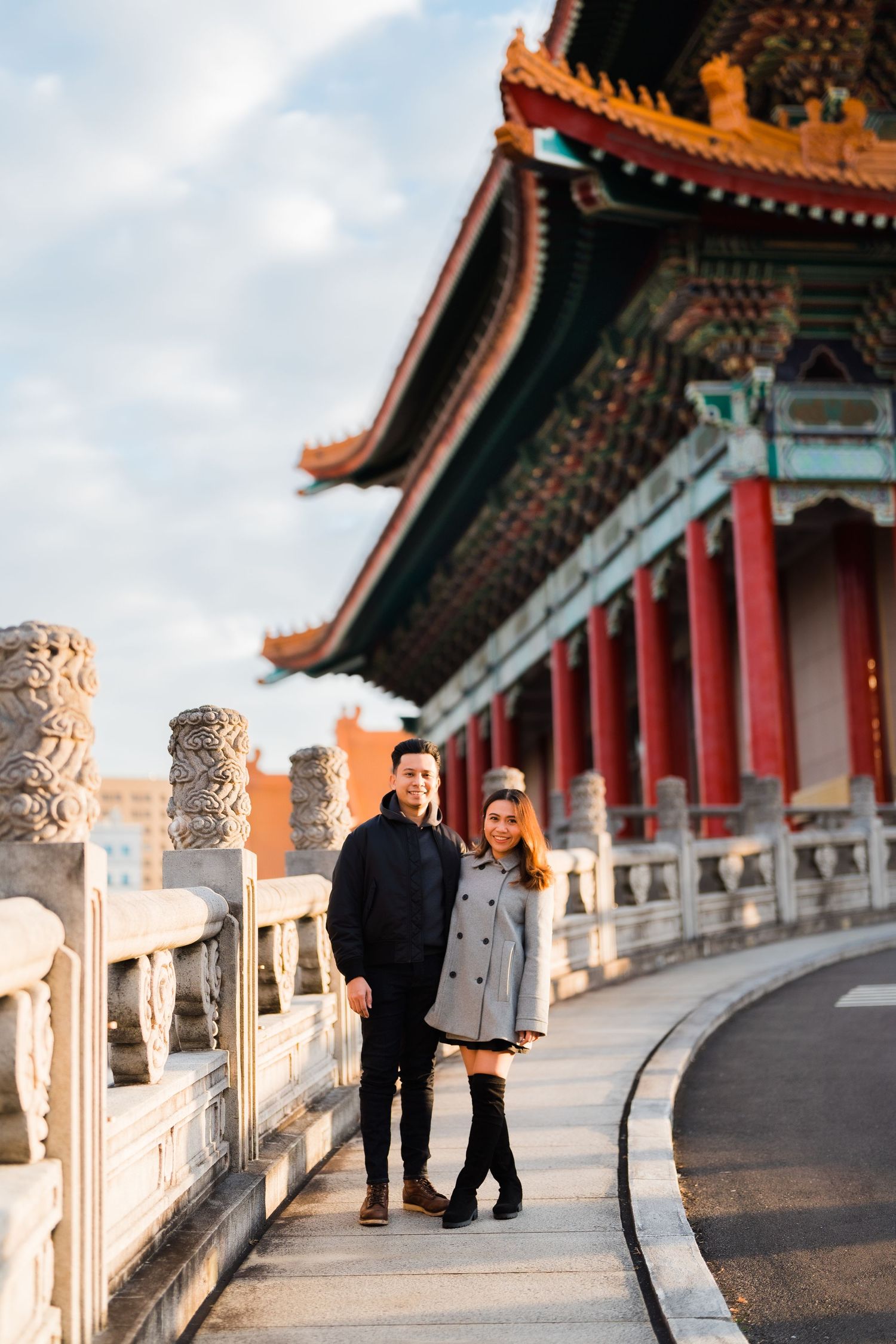 Couple posing together on a curved walkway outside an ornate Asian temple building.