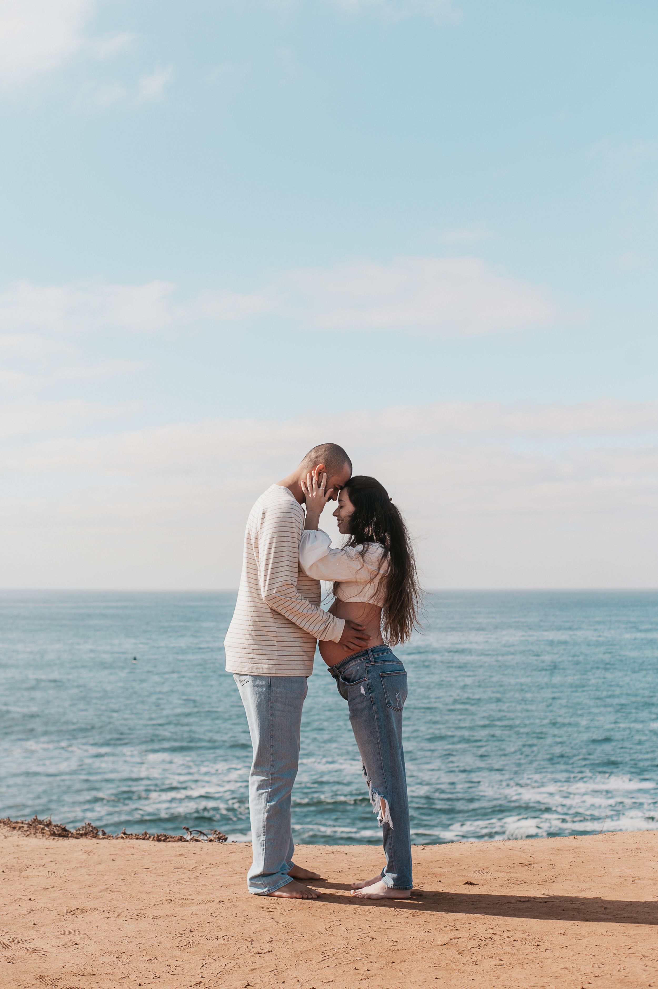 Couple sharing a tender moment on a cliff overlooking the ocean.