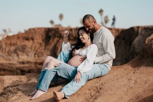 Two people sitting together on coastal rocks during golden hour at the beach.