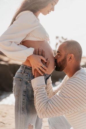 Intimate maternity moment captured on sunny beach with ocean backdrop.