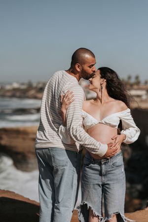 Romantic coastal photoshoot with couple in matching casual outfits by ocean cliffs.