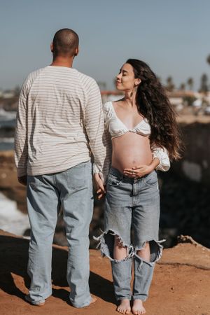 Two people in matching denim and white outfits standing together on coastal cliffside.