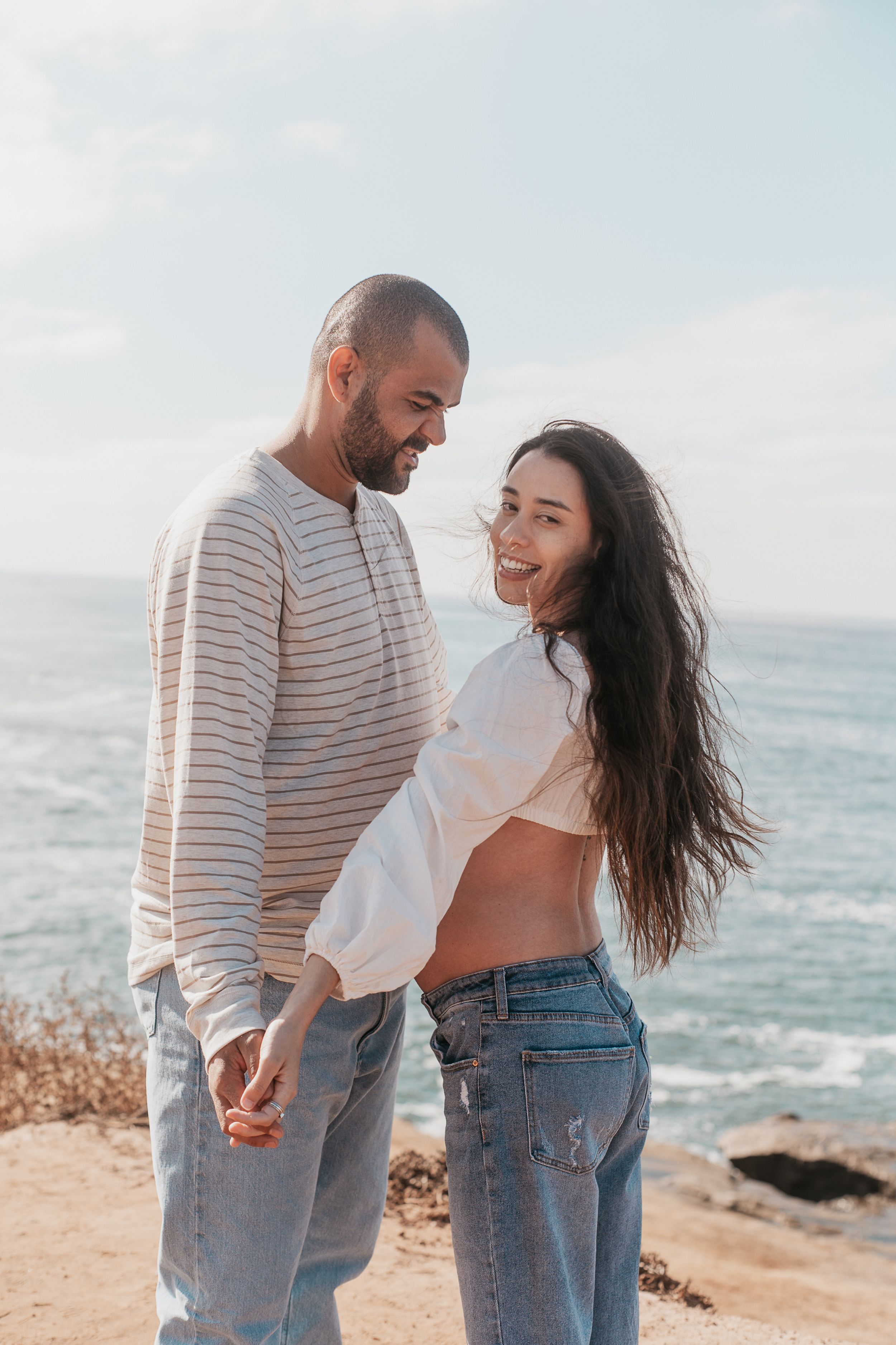Candid photos of a couple laughing and dancing on a coastal cliff.