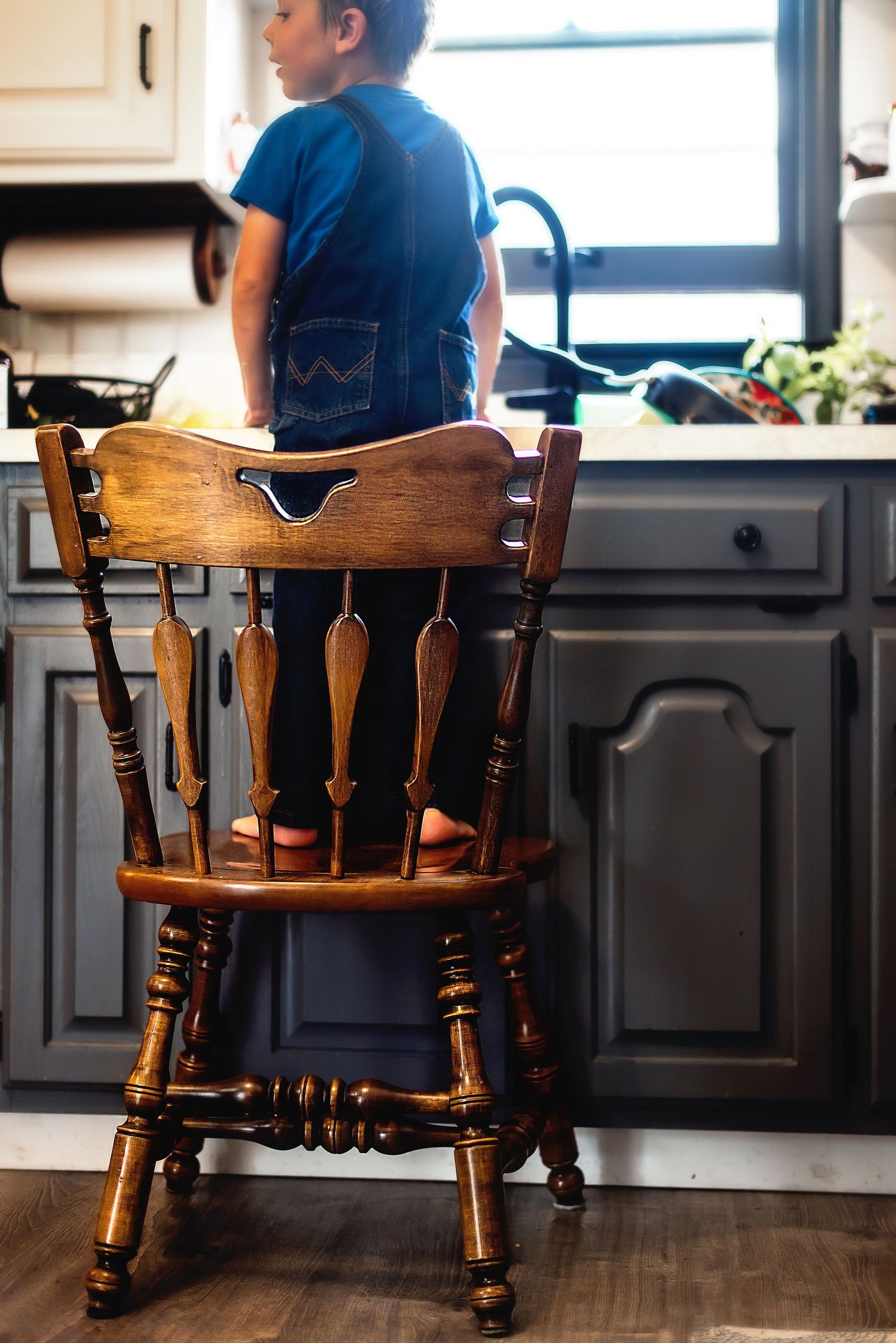 View of a wooden vintage chair in a kitchen with dark cabinets and natural window light.