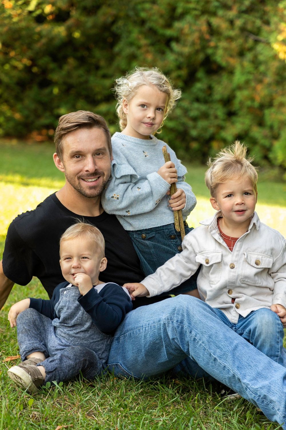 A dad sitting on the grass with his three children all around him located in orono ontario