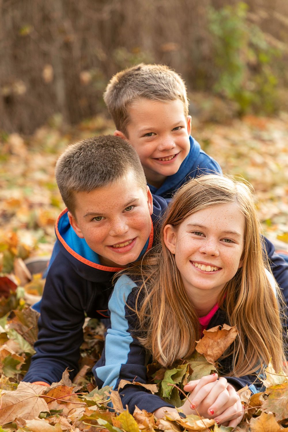 3 kids lying on top of one another in a pile of fall leaves at the Oshawa Botanical Gardens during a sunset