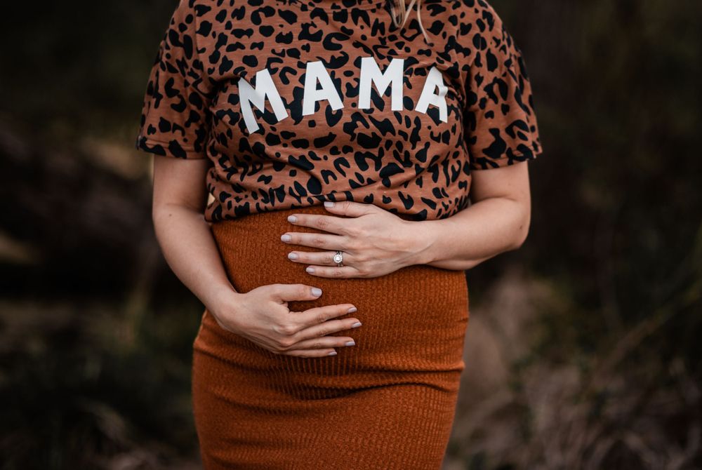 Close up of leopard print shirt with 'MAMA' text and hands on belly.