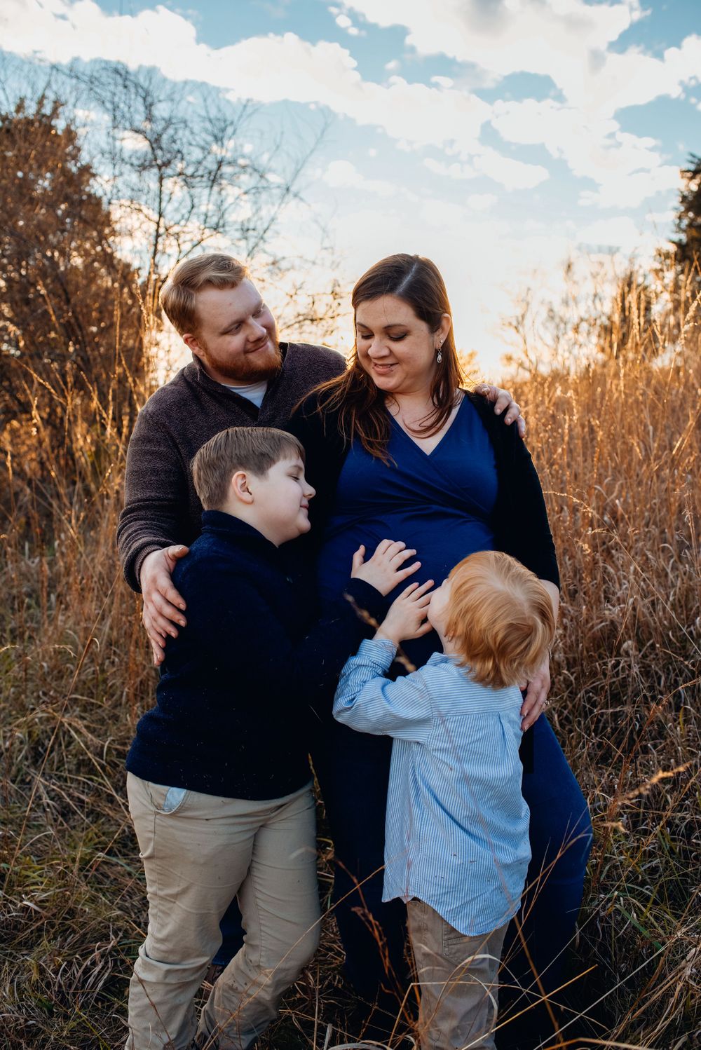 Family gathers in autumn field during sunset maternity photoshoot.