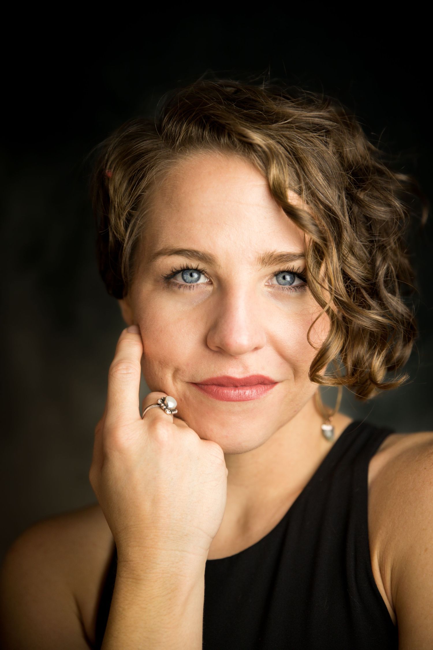 Artistic headshot with dramatic lighting showing curly hair and ring detail.
