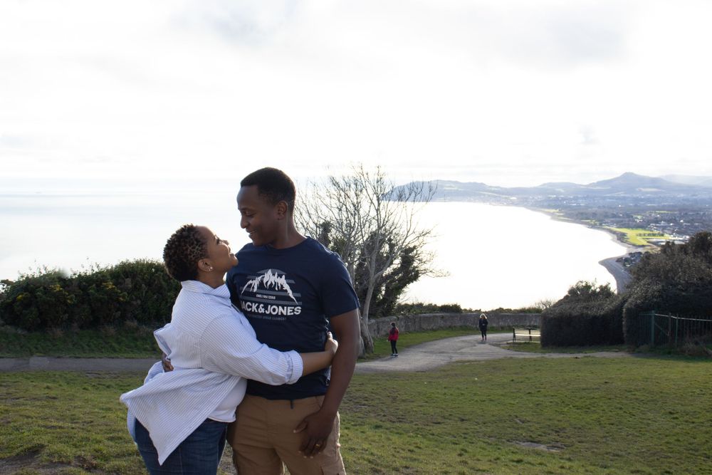 A man and a woman hold each other with a view of the bay in the background