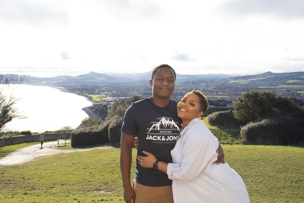A man and a woman hold each other with a view of the bay in the background