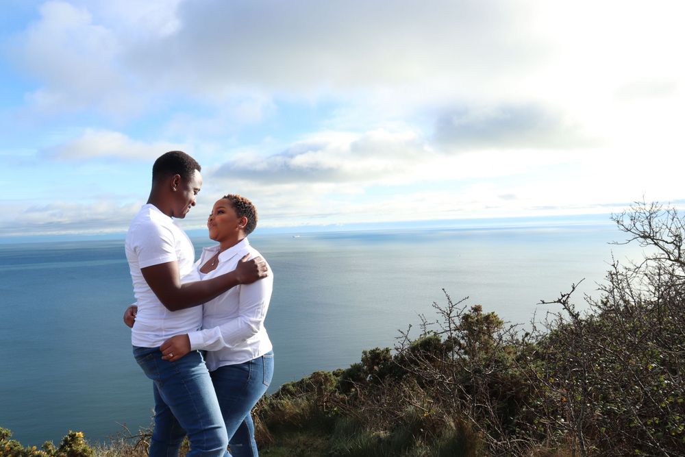 A man and a woman hold each other with a view of the bay in the background