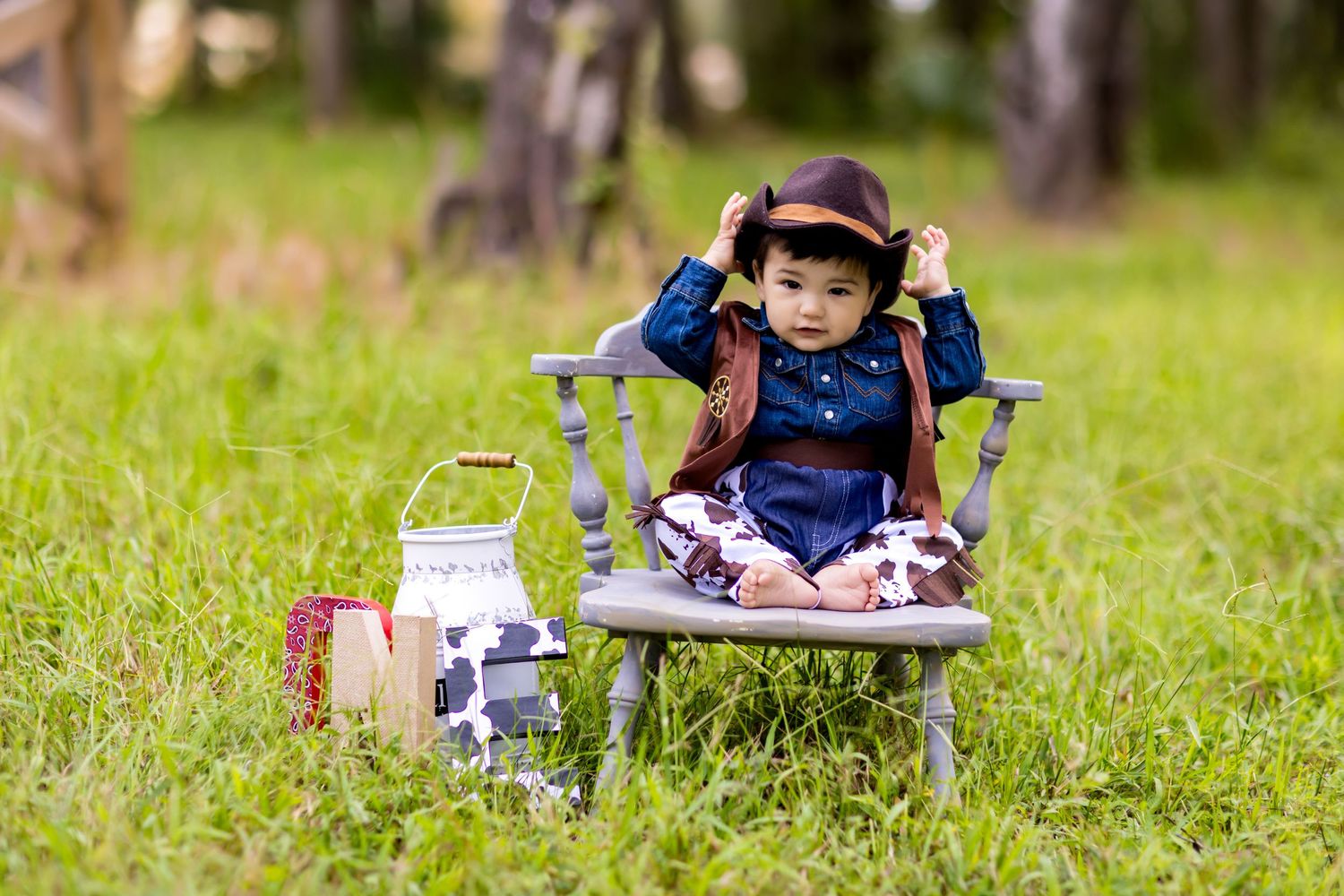 Small child in western wear sits on folding chair with milk jugs in outdoor setting.