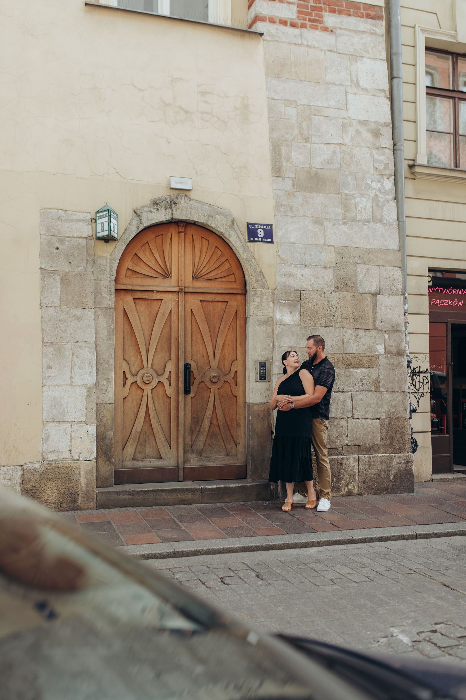 A romantic moment captured near a vintage wooden door against a stone wall in an old European street.