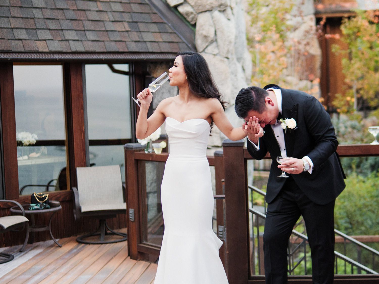 A couple shares a champagne toast on an outdoor deck during a wedding celebration in autumn.