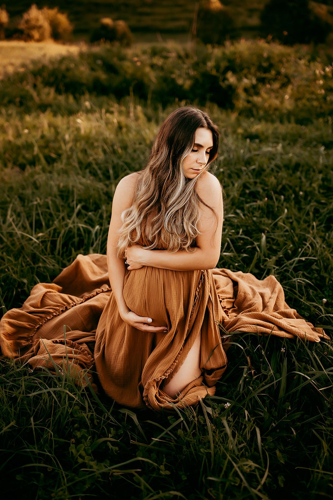 A mother sits on her knees hugging her baby bump during her maternity session in Charlottesville.