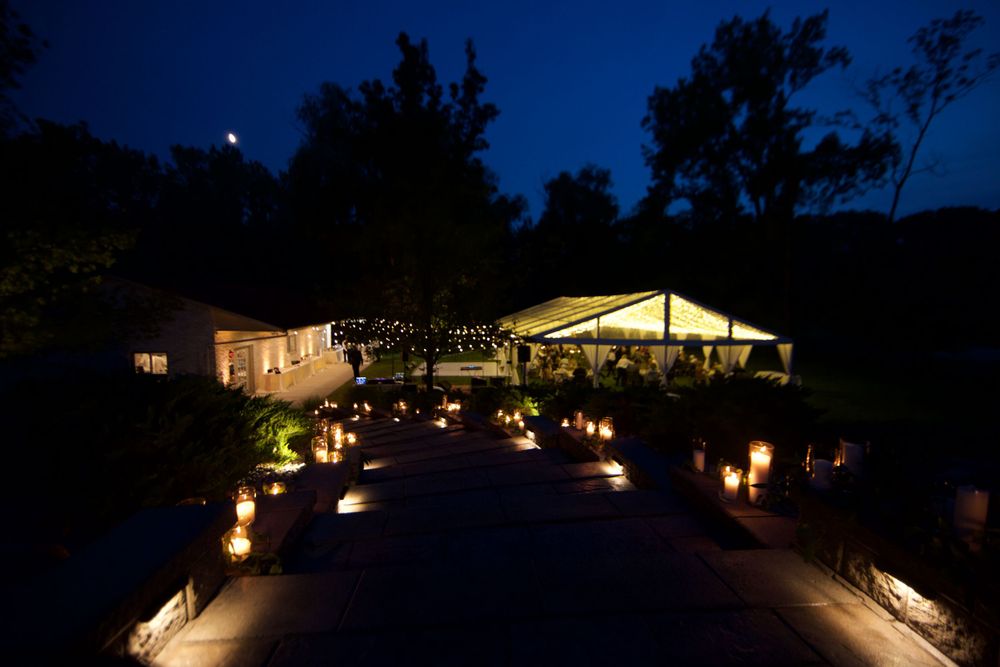 Illuminated pathway at night leads to two lit buildings with string lights creating a romantic ambiance.