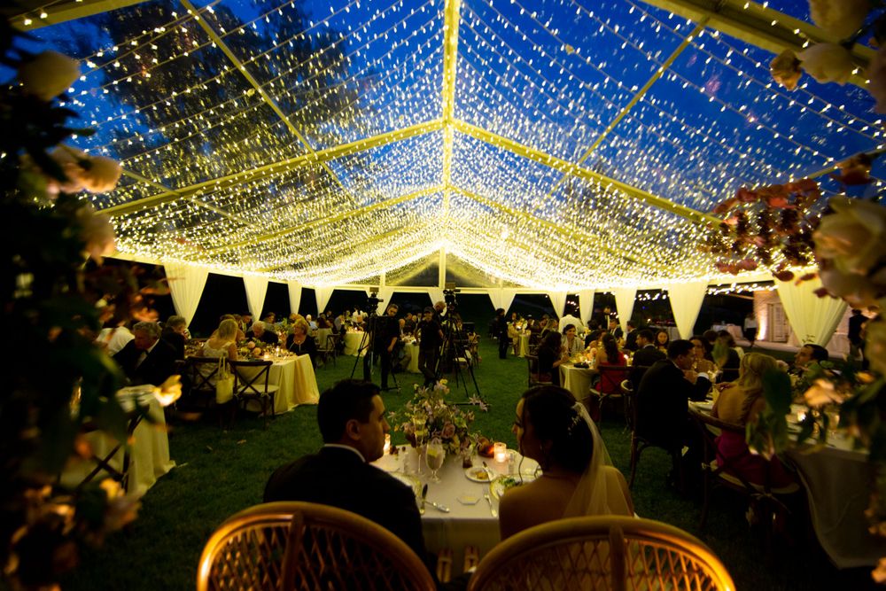 An outdoor wedding reception under a tent ceiling adorned with thousands of twinkling string lights.
