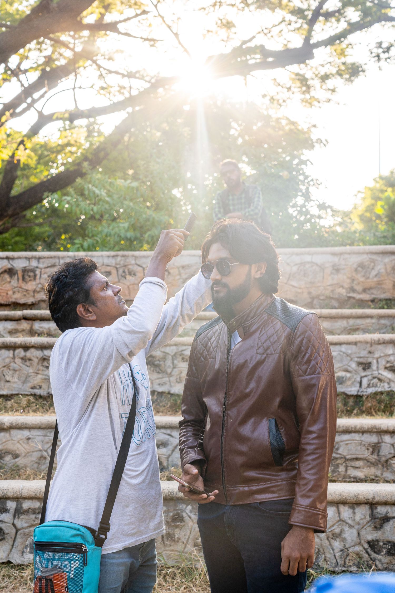 Two people working on a film set with sunlight streaming through trees in the background.