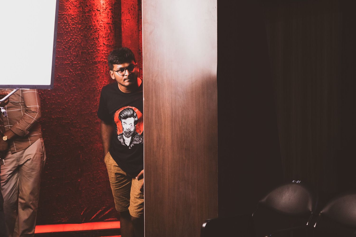 Person in black t-shirt standing against a red wall in dim lighting.