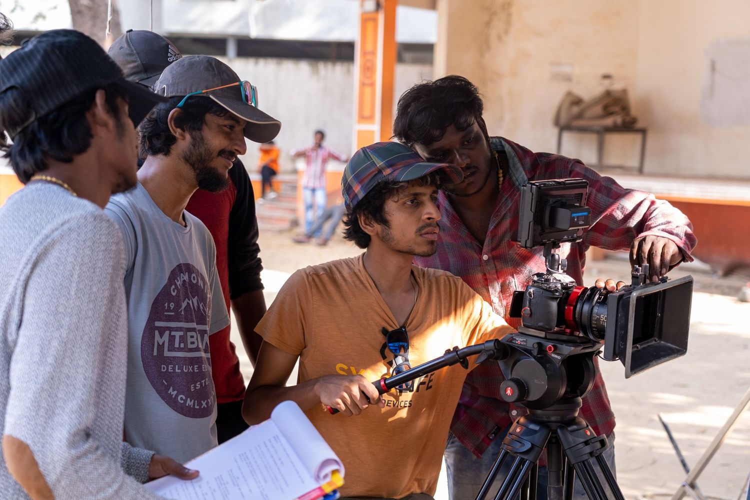 Film crew members gather around a camera to review footage during an outdoor shoot in bright daylight.
