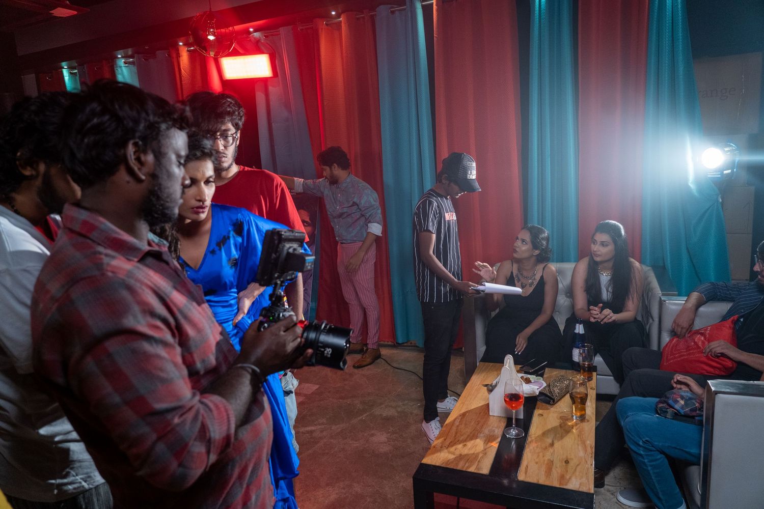 Camera operators film a scene in a studio space with red and blue lighting effects.