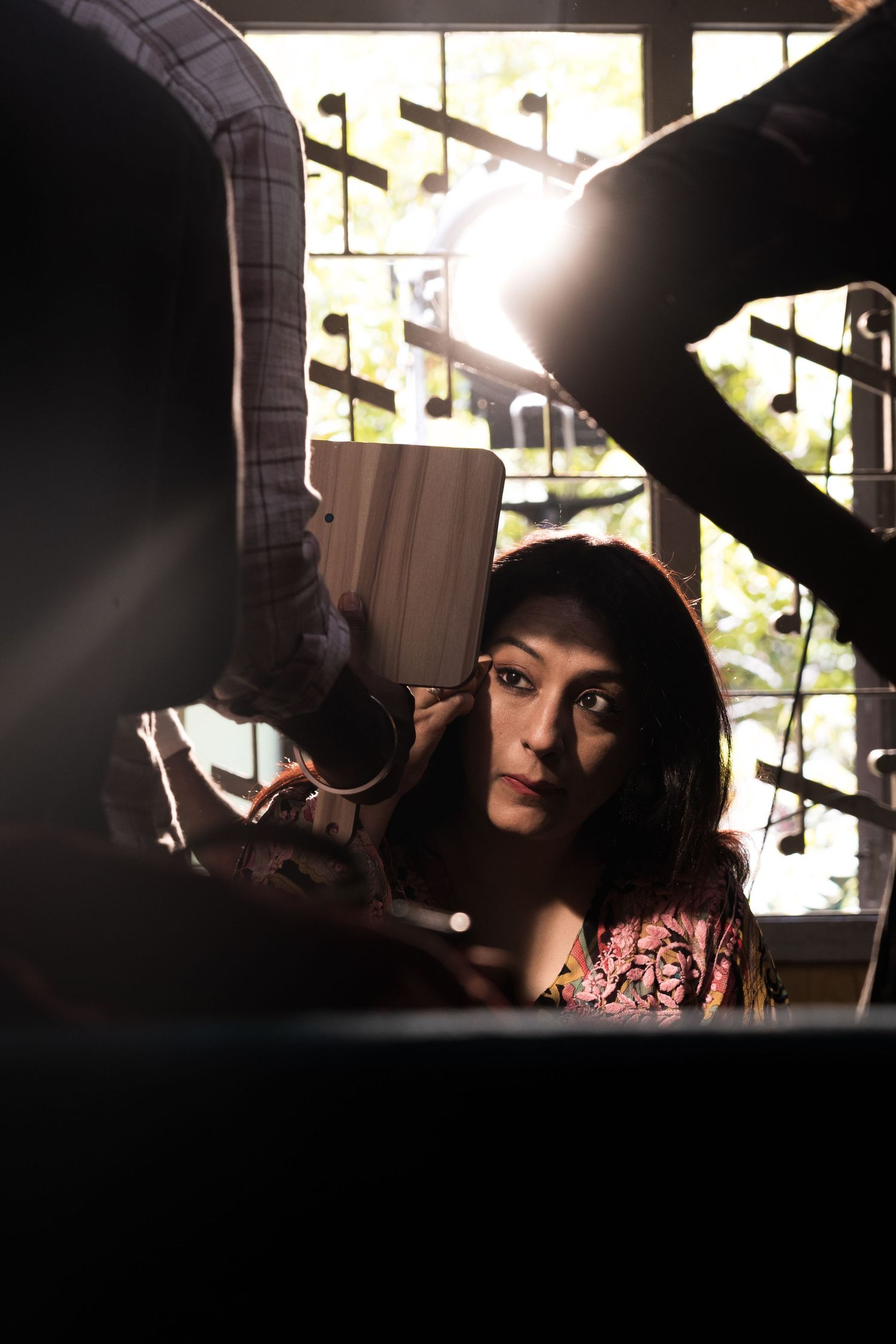 Artistic portrait shot through window panes with dramatic backlighting and decorative elements.