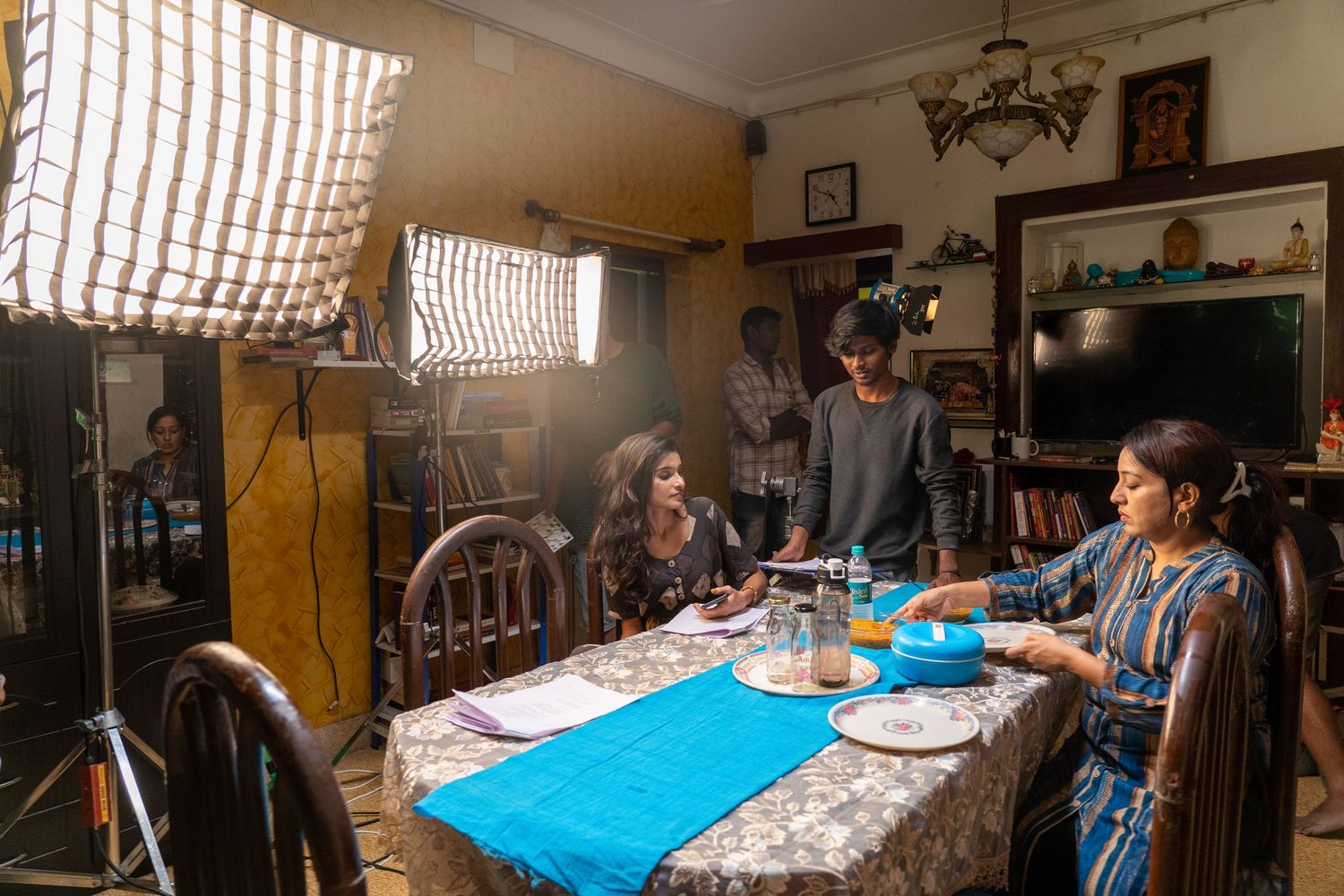 Film production crew works on a scene at a dining table with professional lighting equipment.