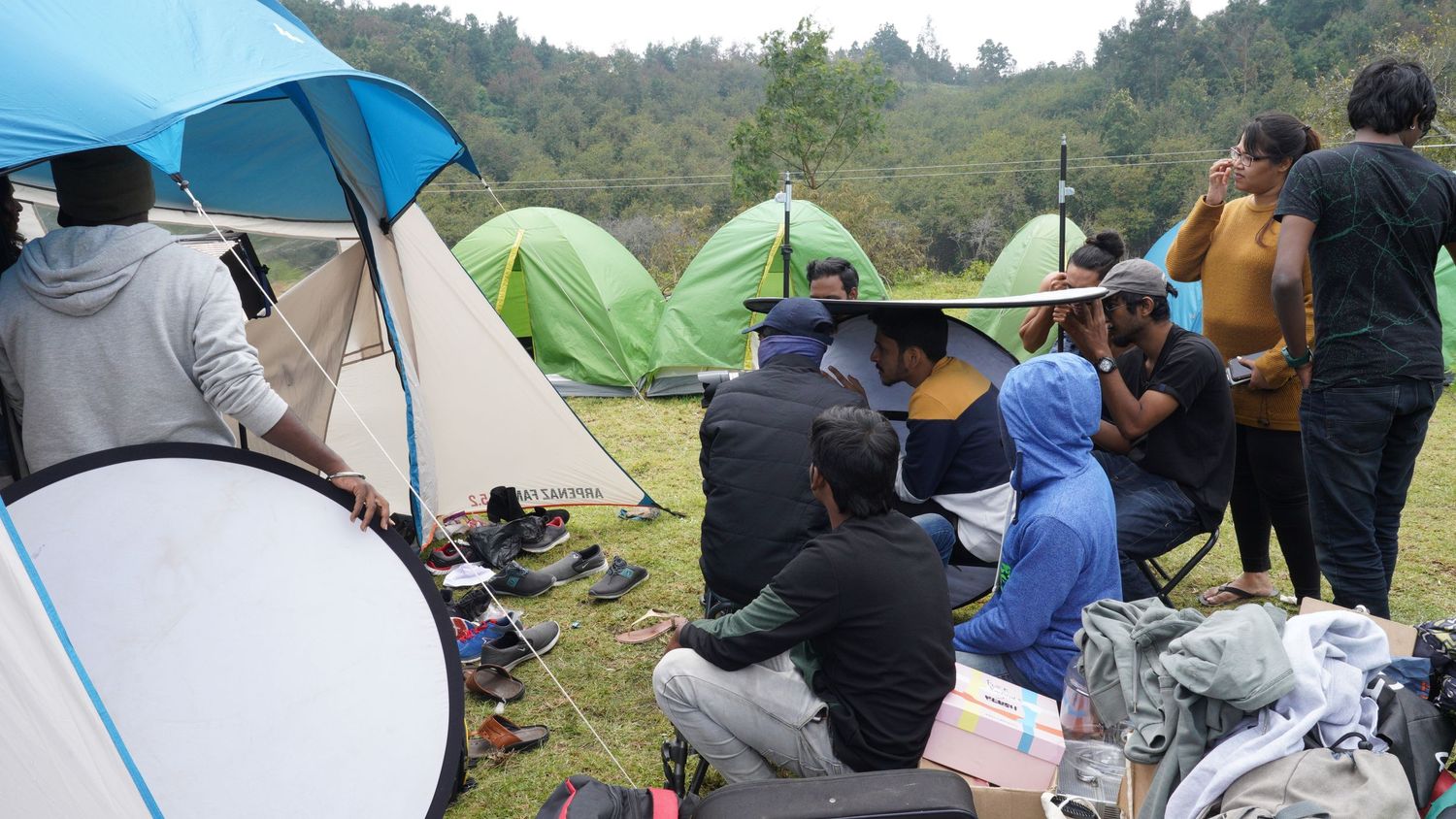 People gathered under blue and green tents on a hillside for an outdoor event.