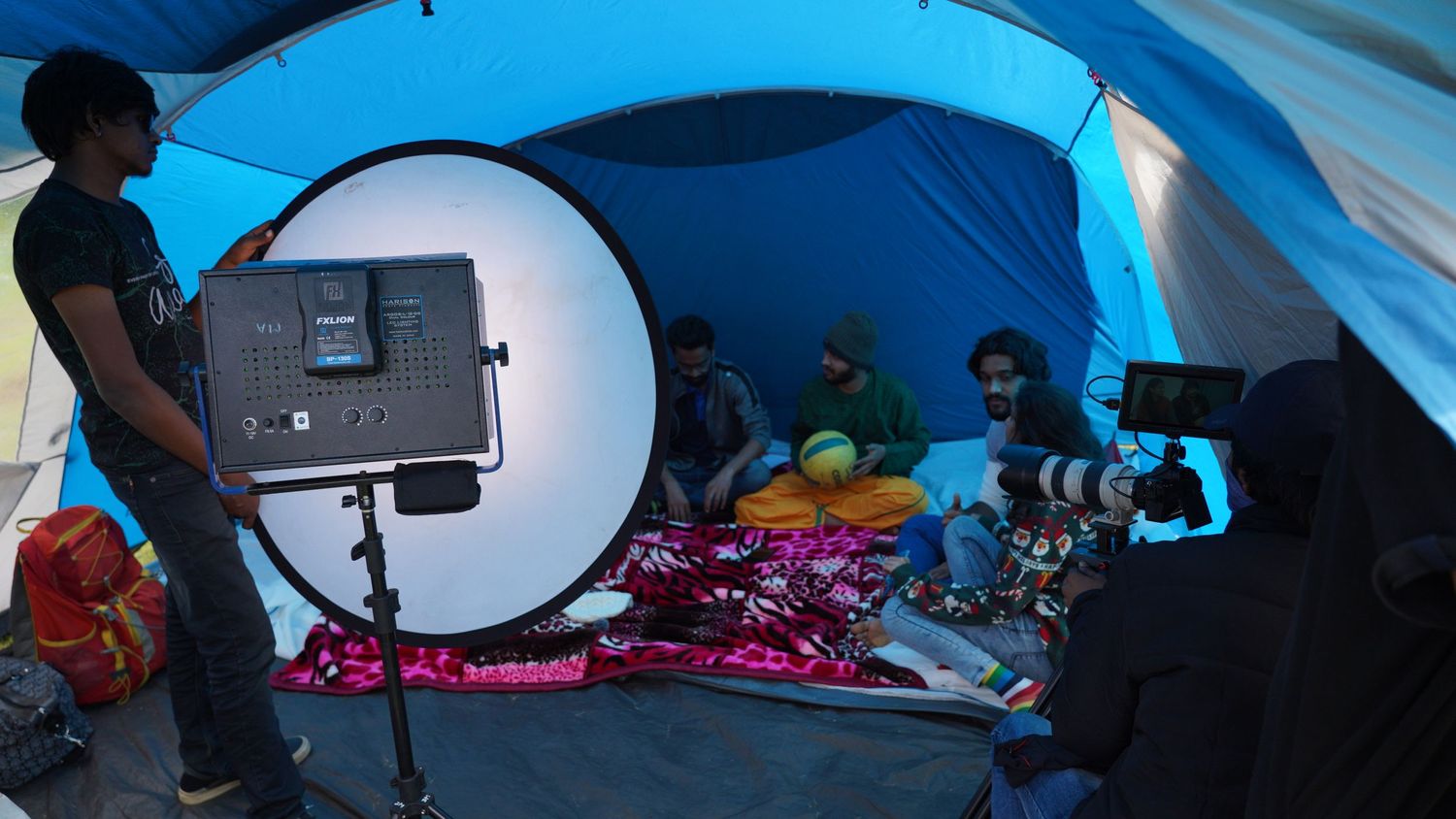 Film production setup inside a blue tent with lighting equipment and crew members.