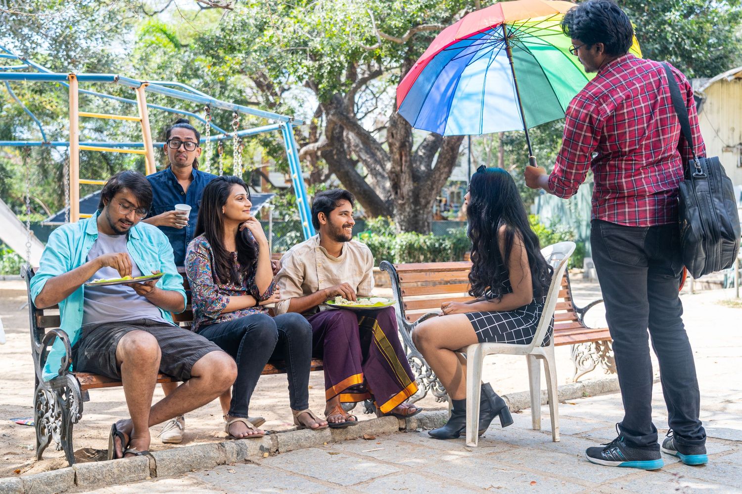 Group of people sitting on benches under colorful umbrellas in an outdoor setting.