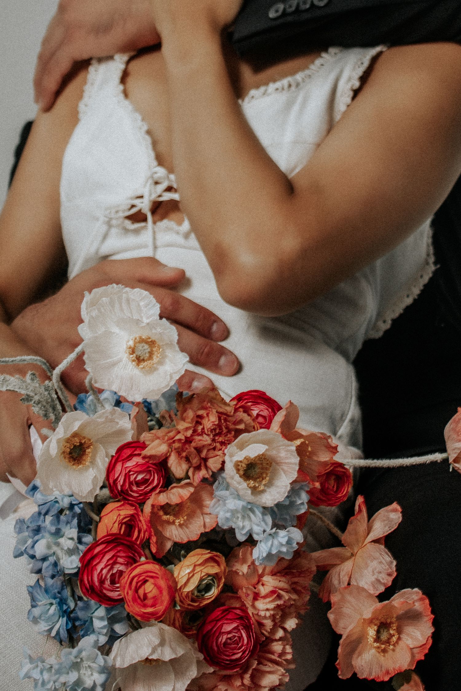 Detailed shot of bridal bouquet with red roses, white flowers and blue hydrangeas against white dress.