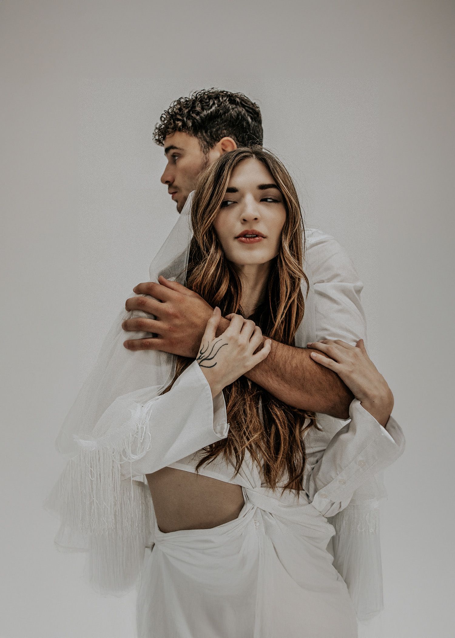 A romantic artistic portrait of a couple embracing in soft white clothing against a minimal background.