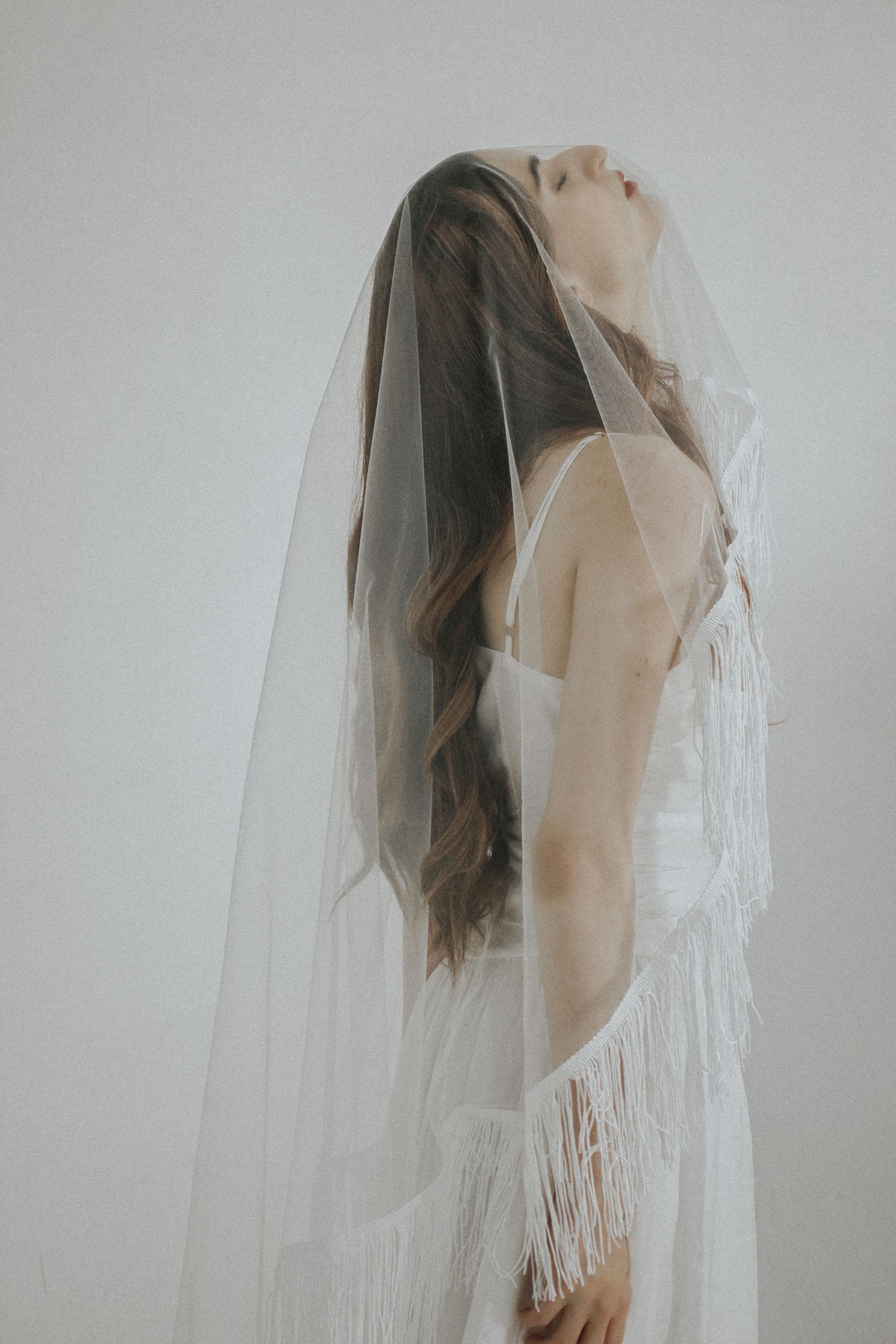 Artistic side profile of figure draped in flowing white veil against light background.