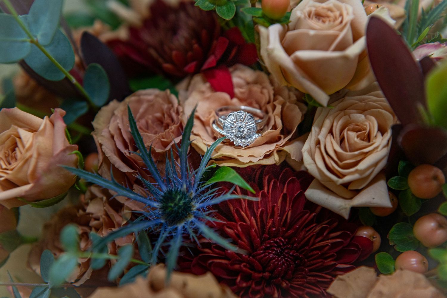 Close-up detail of burgundy and blush wedding flowers with textural elements and greenery.
