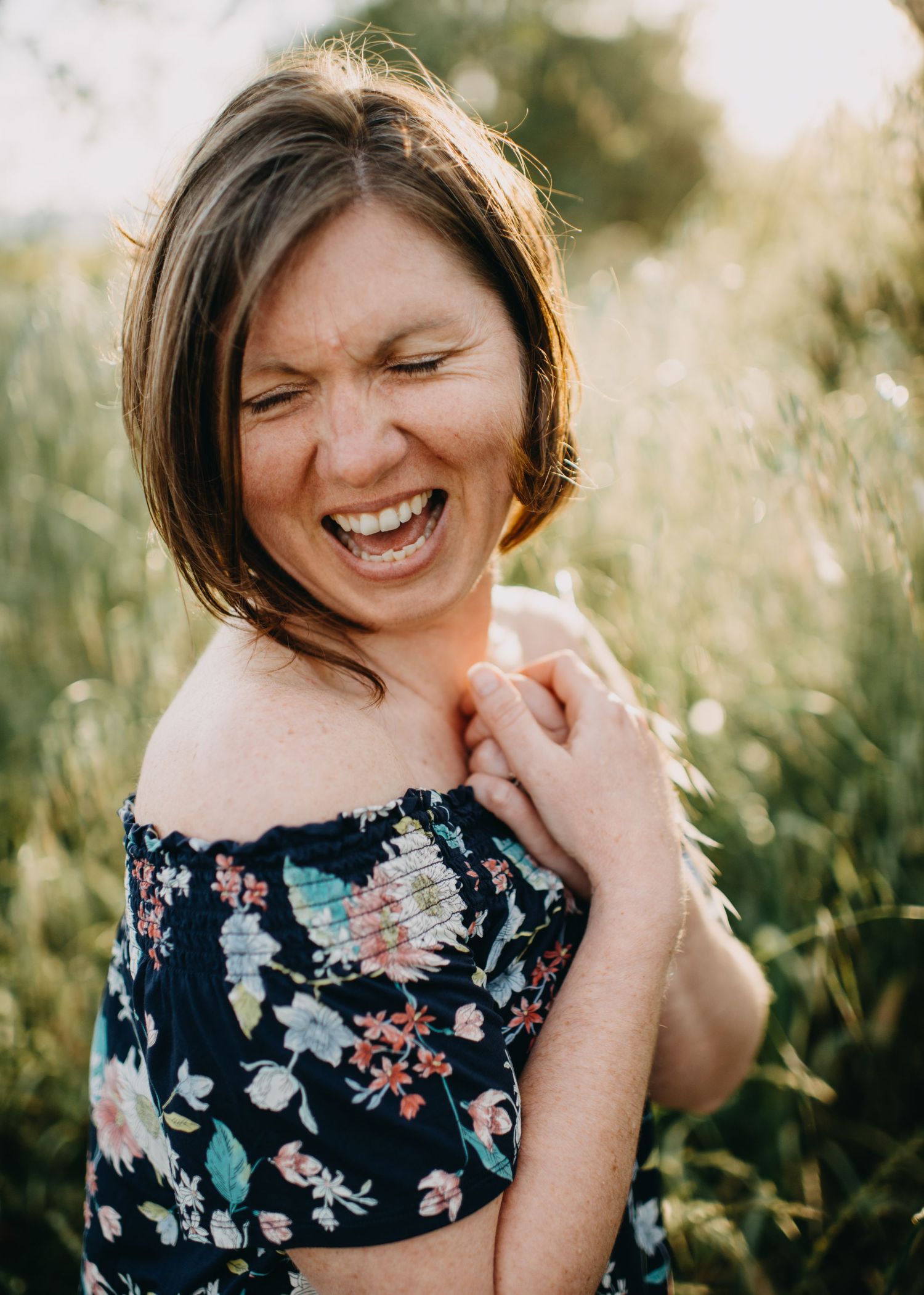 Candid portrait showing joyful laughter in a floral off-shoulder dress against a sunlit natural outdoor setting-Alexis Anne Photography