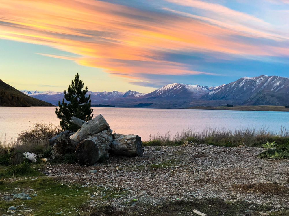 Stunning sunset sky over Lake Tekapo with vibrant orange clouds reflecting on the calm water surface.