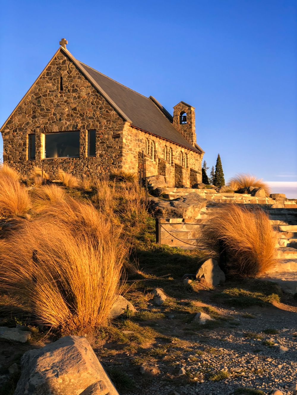 Historic stone church with tussock grass in foreground during golden hour.