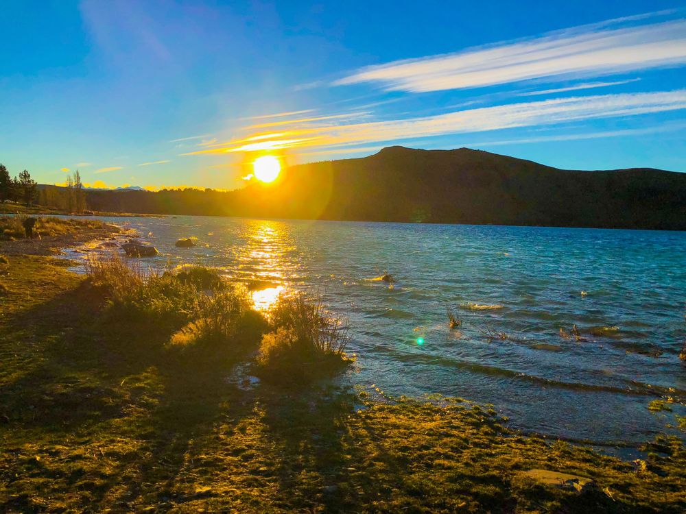 Panoramic sunset view over Lake Tekapo with mountains in the background.