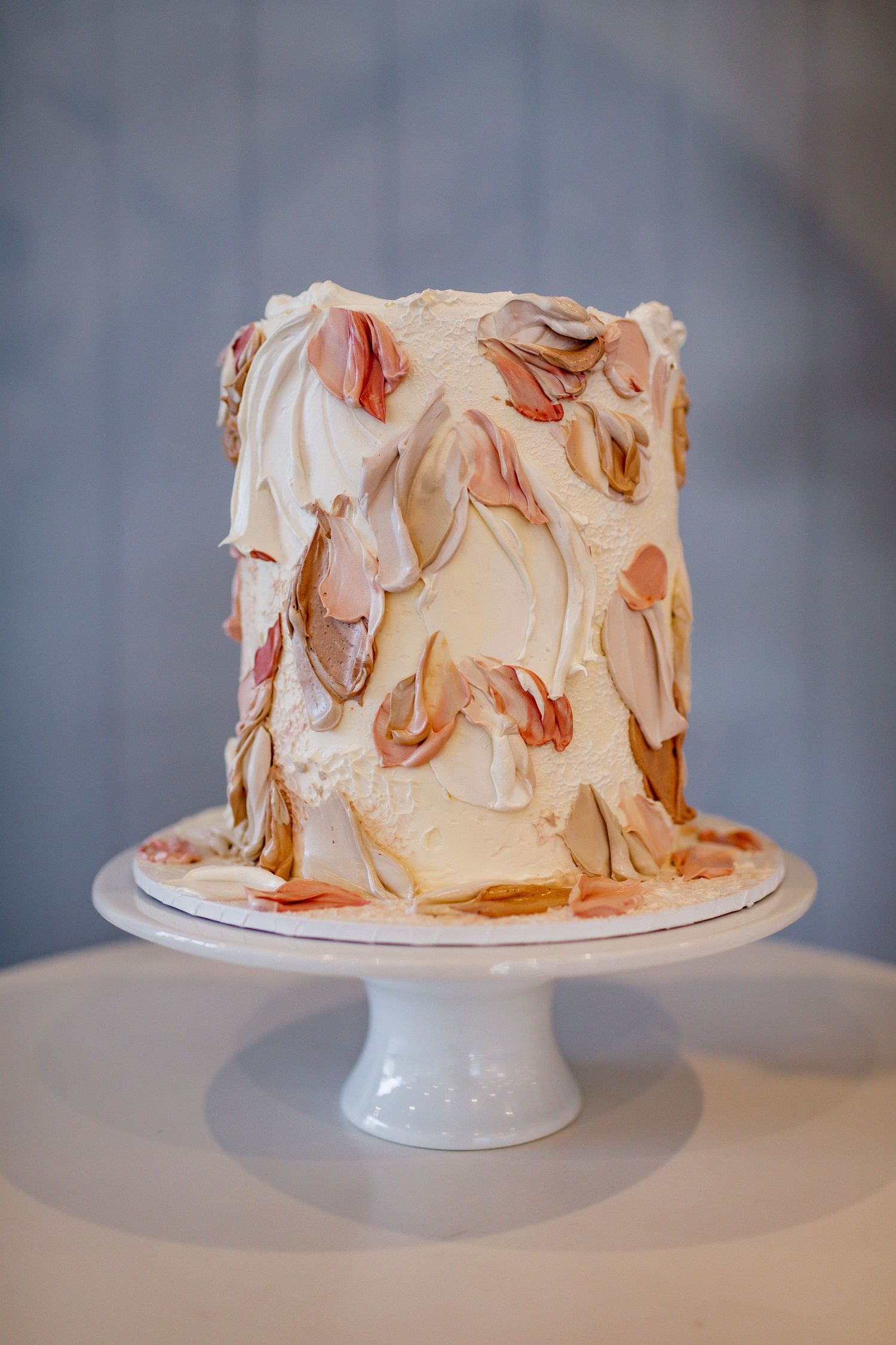 Modern textured wedding cake with peach and cream colored abstract designs on white cake stand.