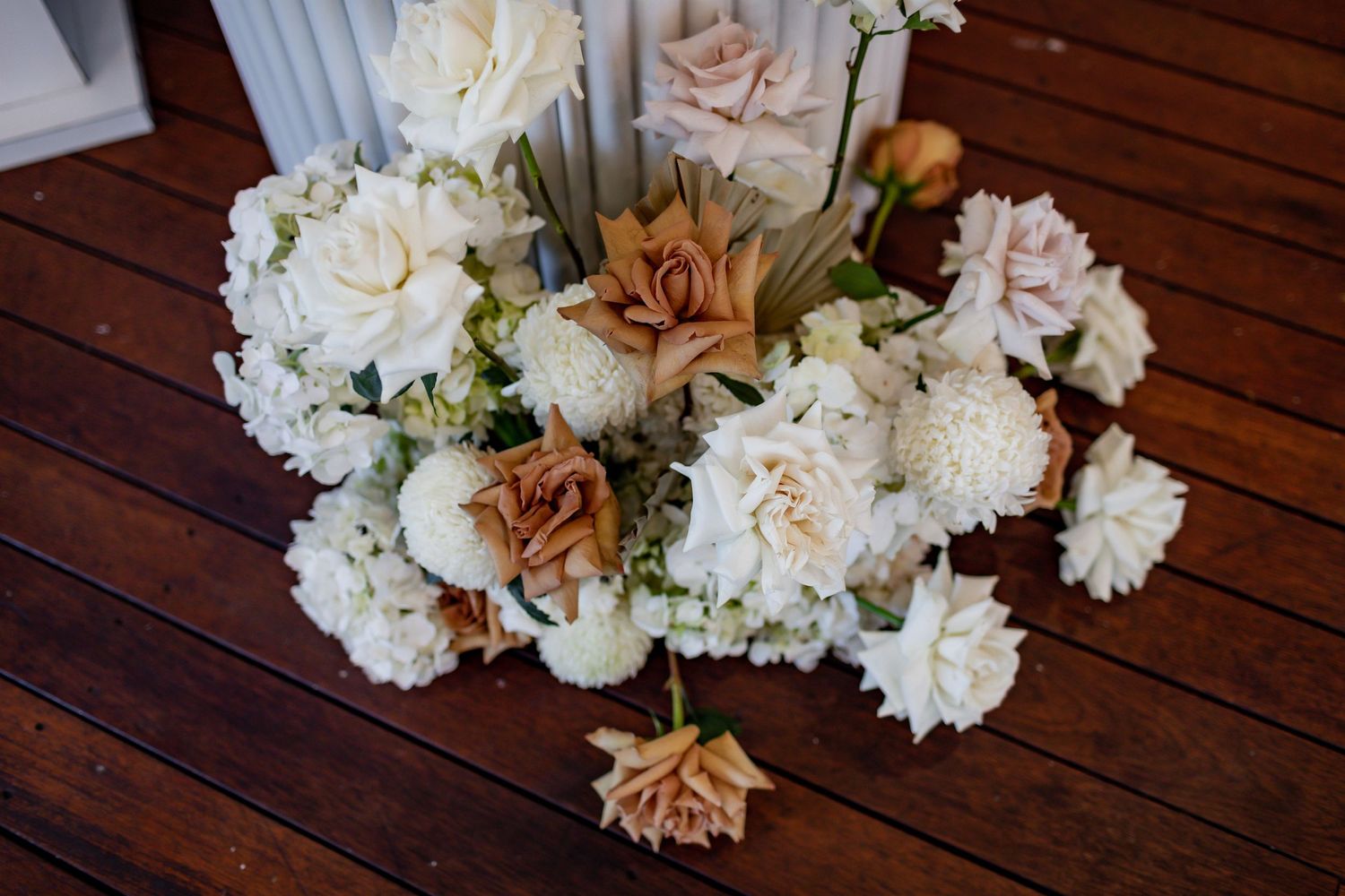 Romantic floral arrangement with peach and white roses on wooden decking.