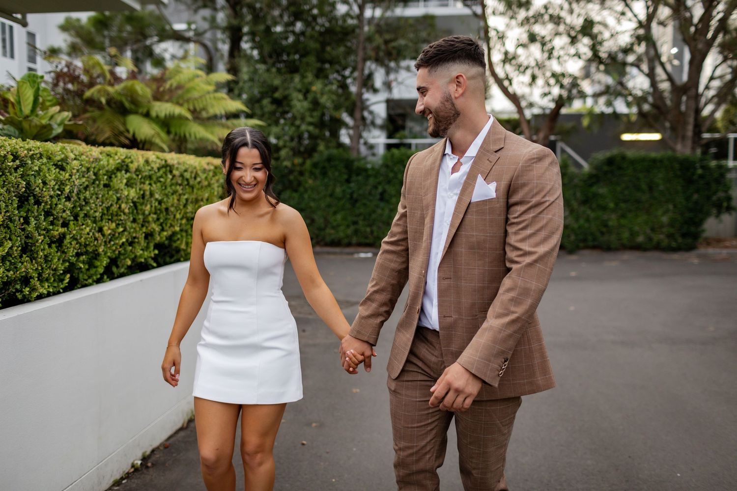 Elegant couple holding hands while walking along a garden path.