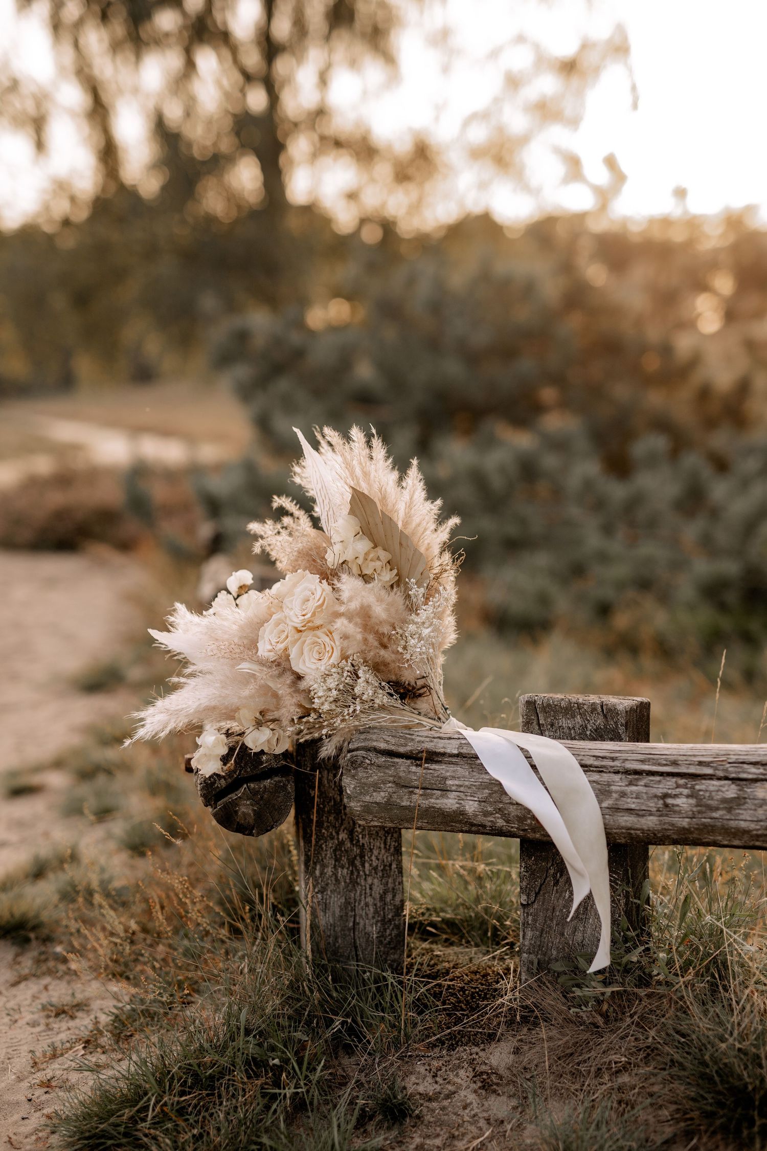 Dried floral bouquet with pampas grass and roses resting on weathered wooden fence.