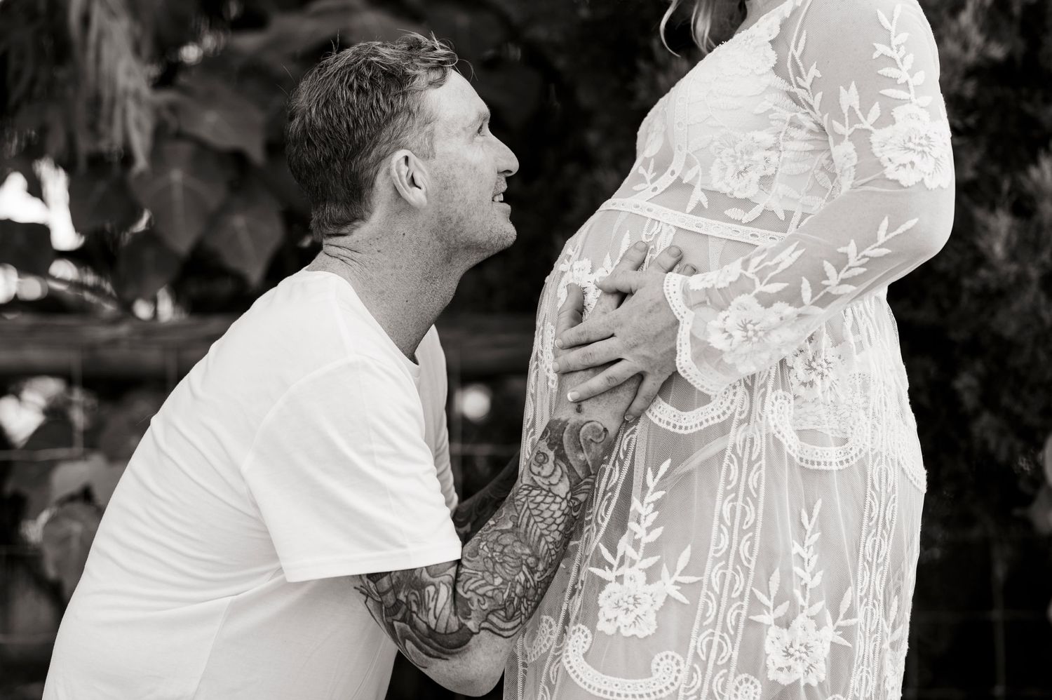 A tender black and white maternity portrait with intricate lace dress details.