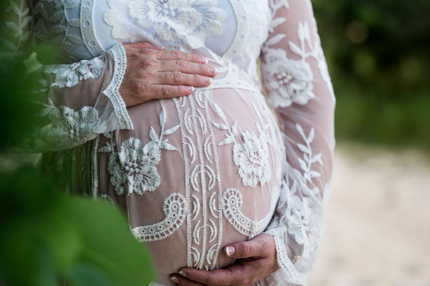 Detailed shot of hands cradling a pregnant belly through delicate lace fabric.