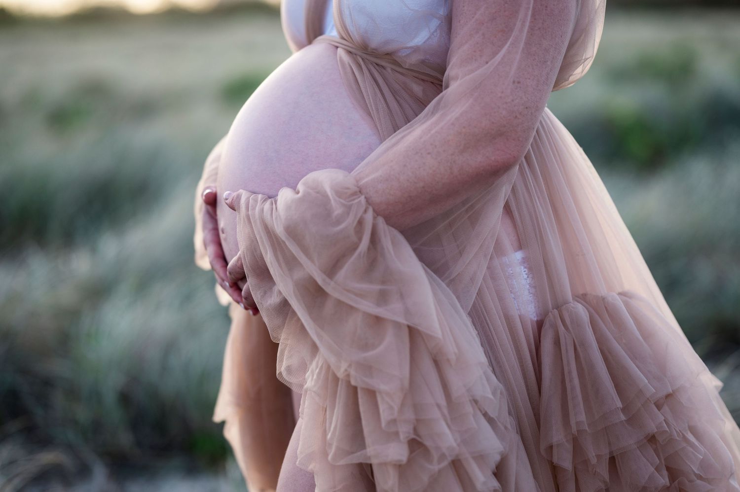 A flowing pink tulle maternity dress photographed in soft natural light.