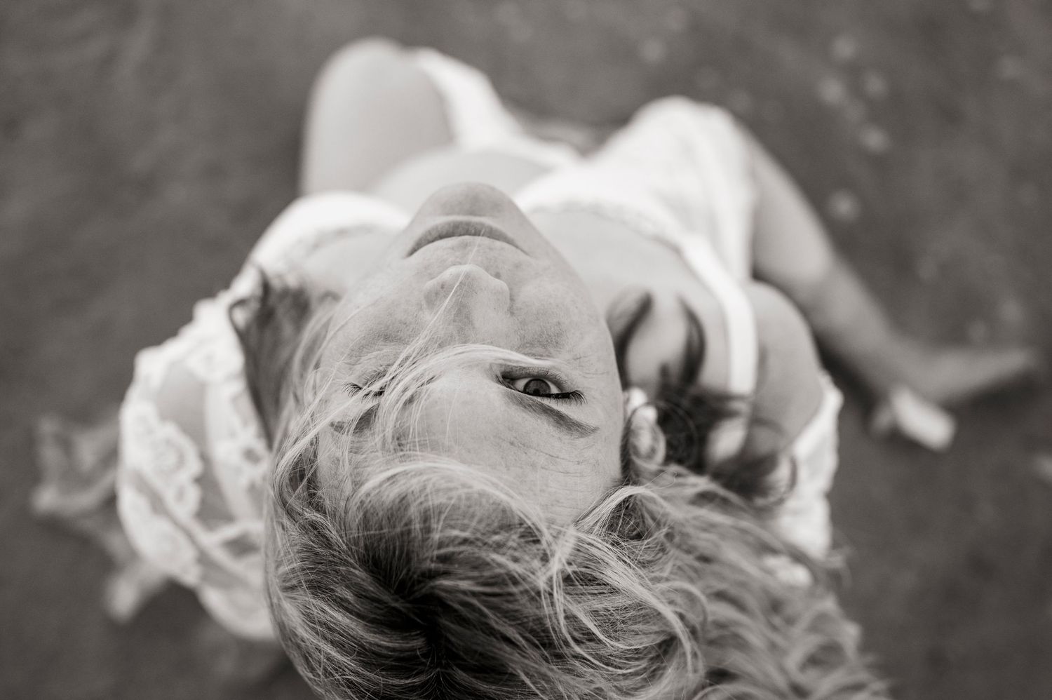 Artistic black and white portrait of someone lying on the ground with dreamy expression.