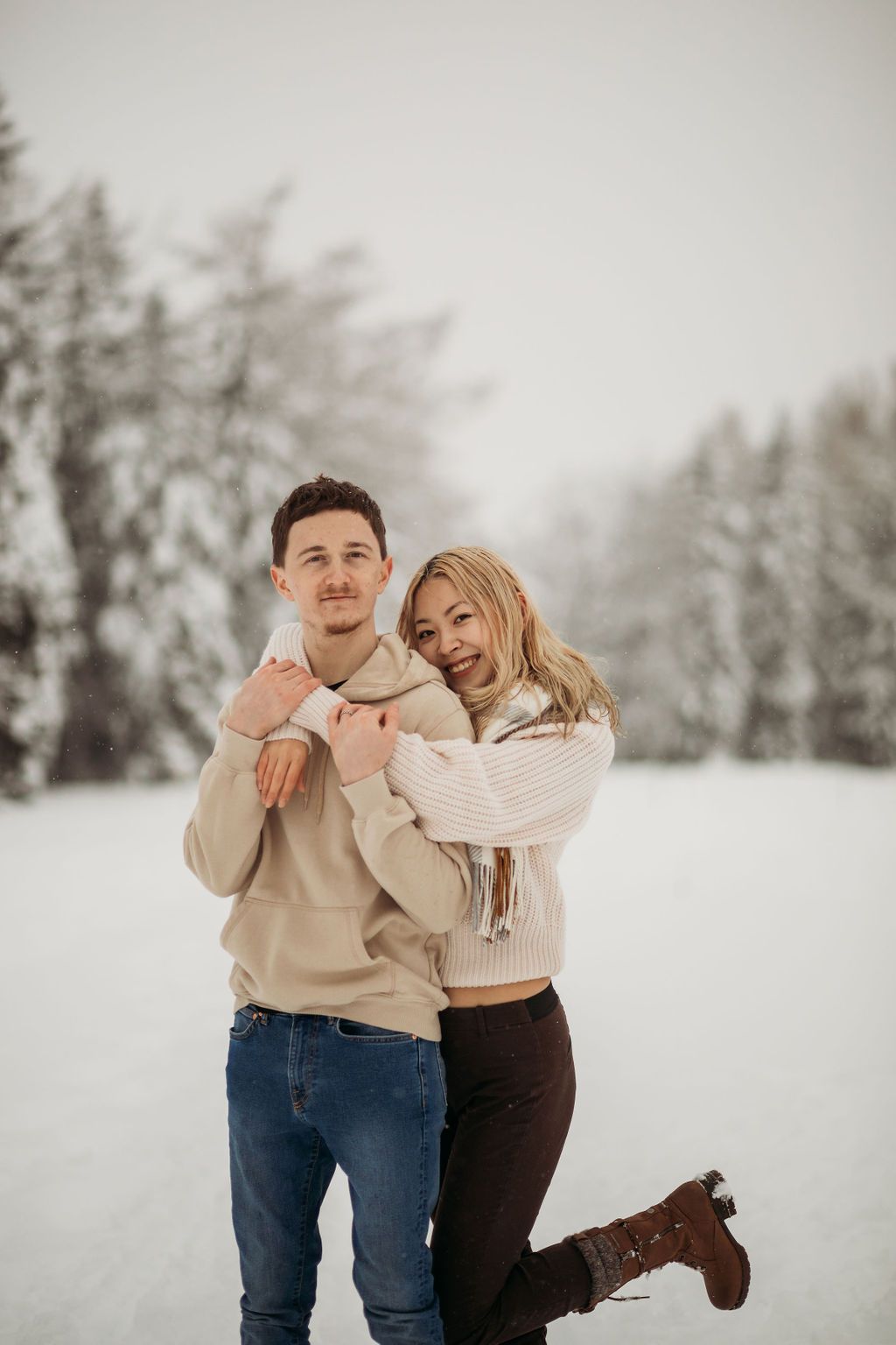 Couple in matching neutral sweaters posing together in a snowy winter setting.