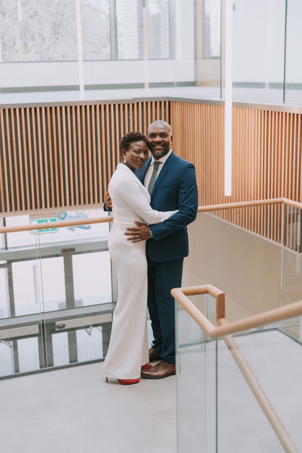 A couple embraces in a modern interior space with wooden accent walls and handrails.