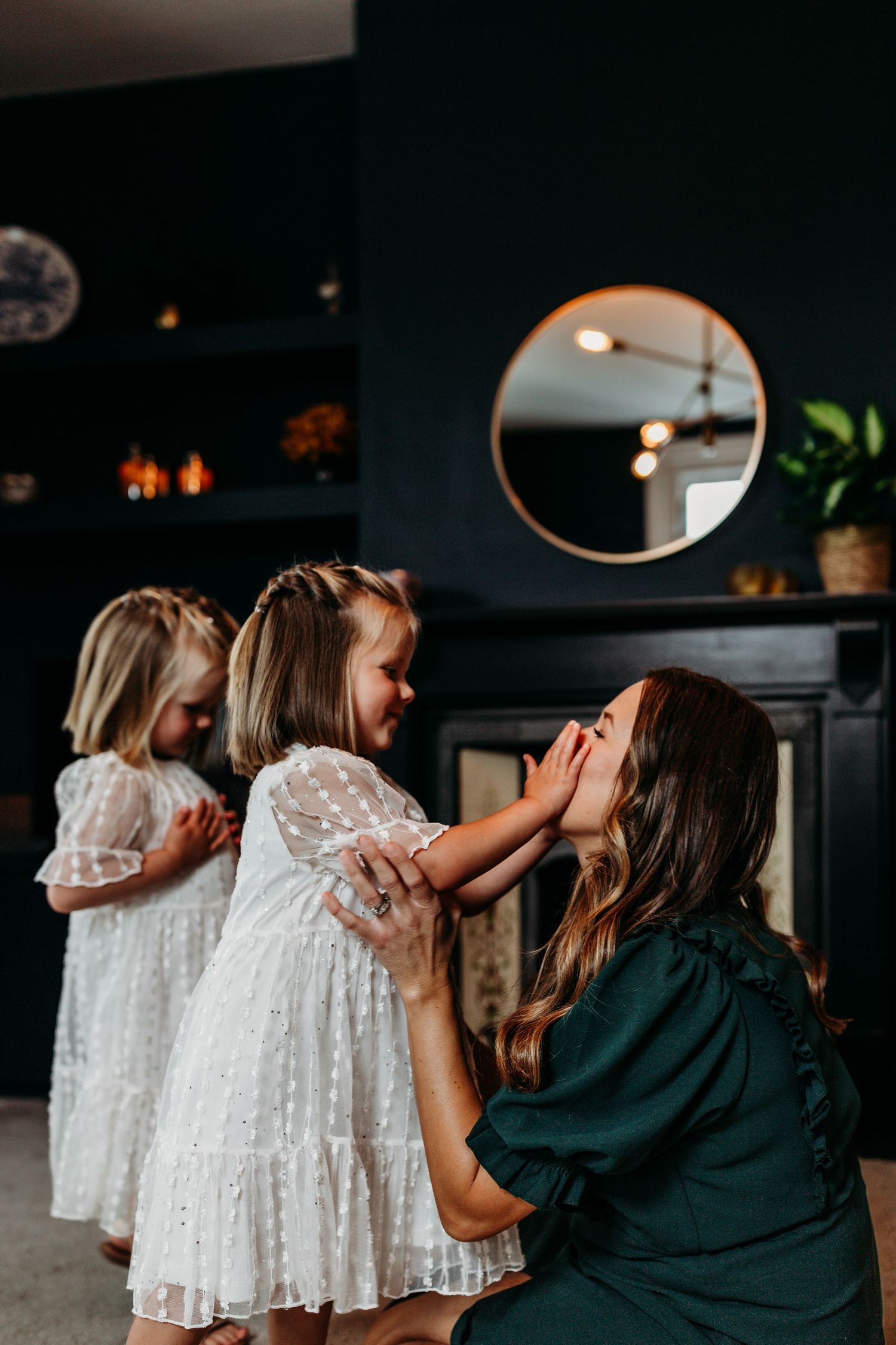 Tender moment shared between family members in white dresses against dark interior.